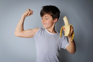 boy flexes while eating banana