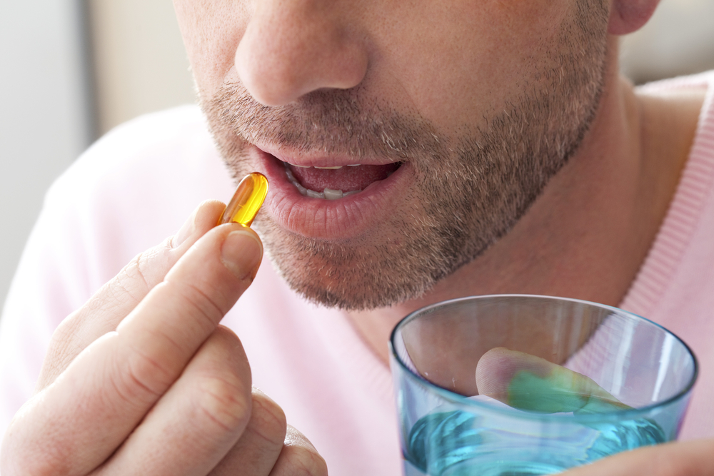 man taking fish oil soft gel capsule