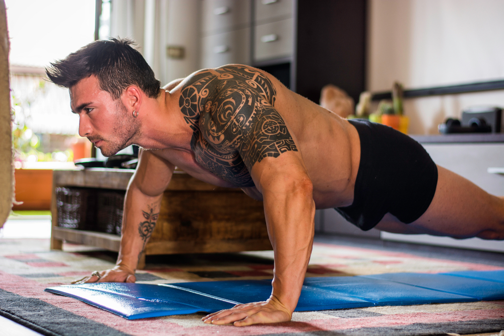 tattooed buff guy doing push ups at home