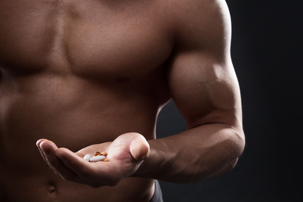 shirtless man holding supplements